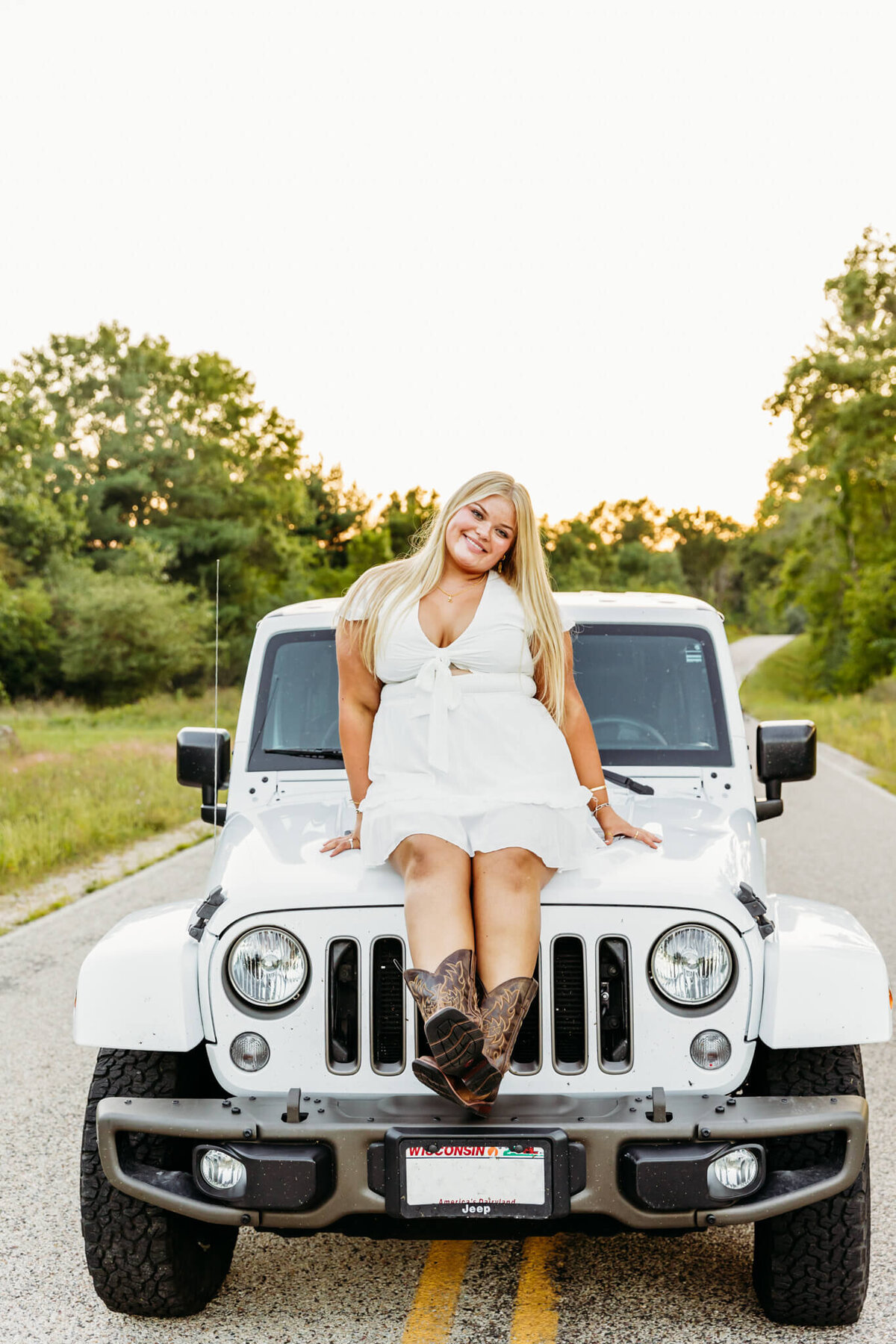 beautiful teenage girl in a white dress and brown cowboy boots sitting on top of her white jeep in the middle of a backroad captured by Ashley Kalbus