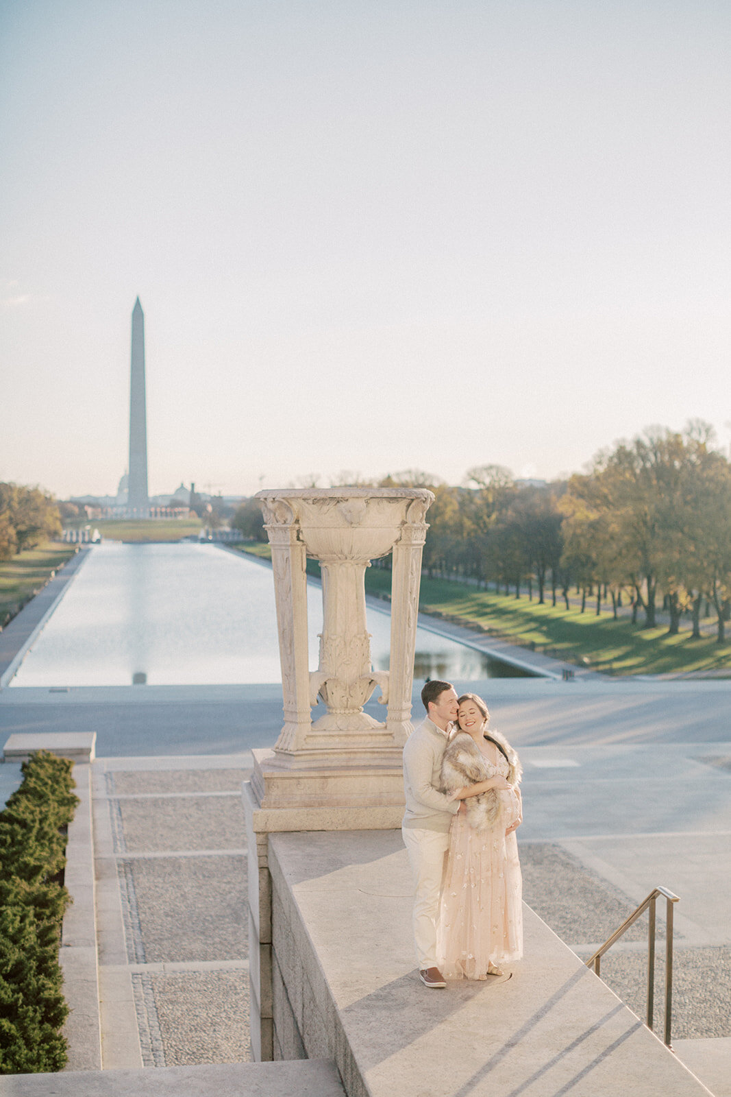 Pregnant mother leans into her husband as they stand in front of the Lincoln Memorial with a view of the Washington Monument during their maternity session.