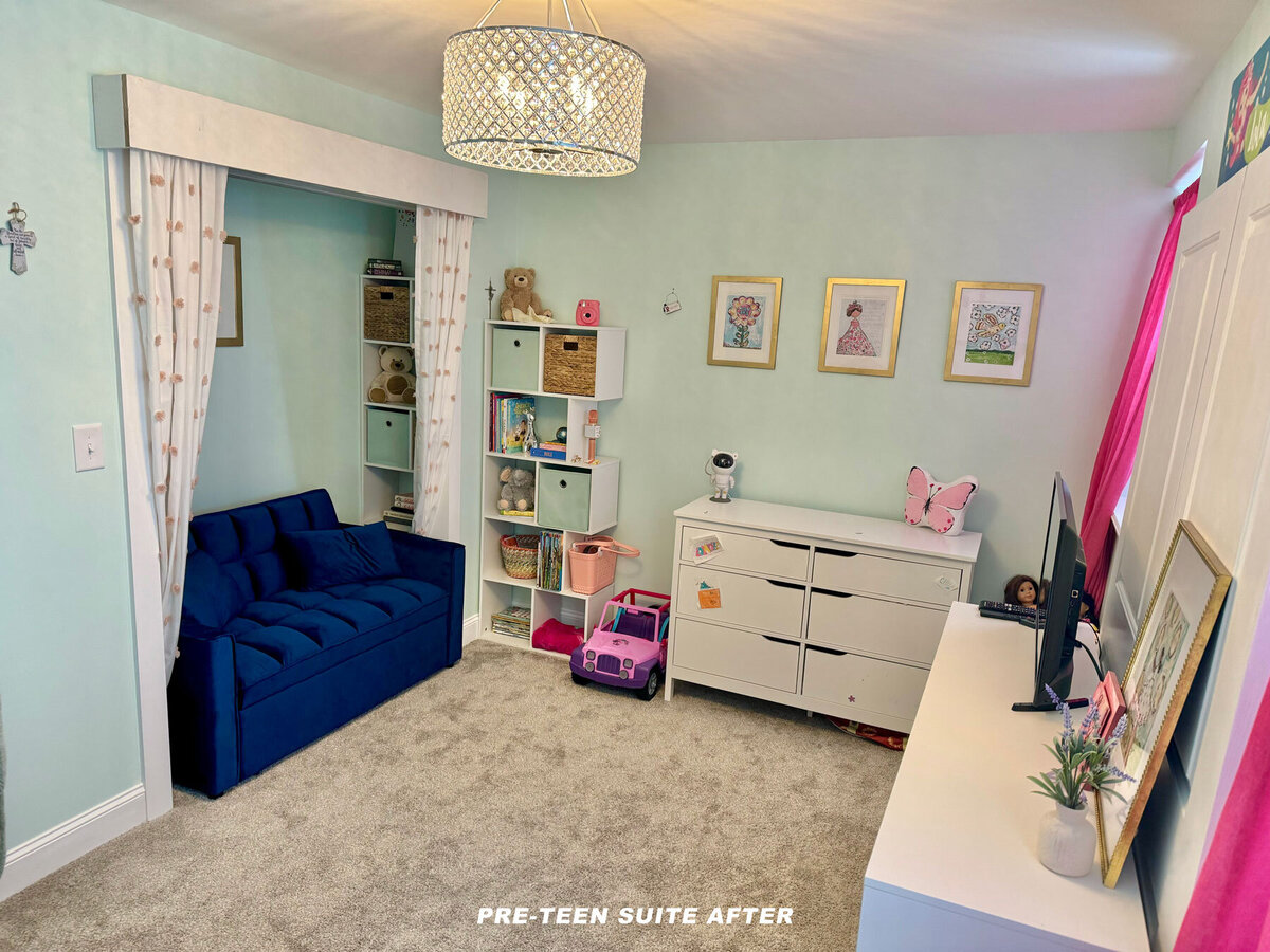 A child's room with a blue couch, white dresser, and colorful storage cubes. Toys and books are neatly arranged. Walls are pale green with framed pictures and curtains decorated with stars. A chandelier hangs from the ceiling. The carpet is light gray.