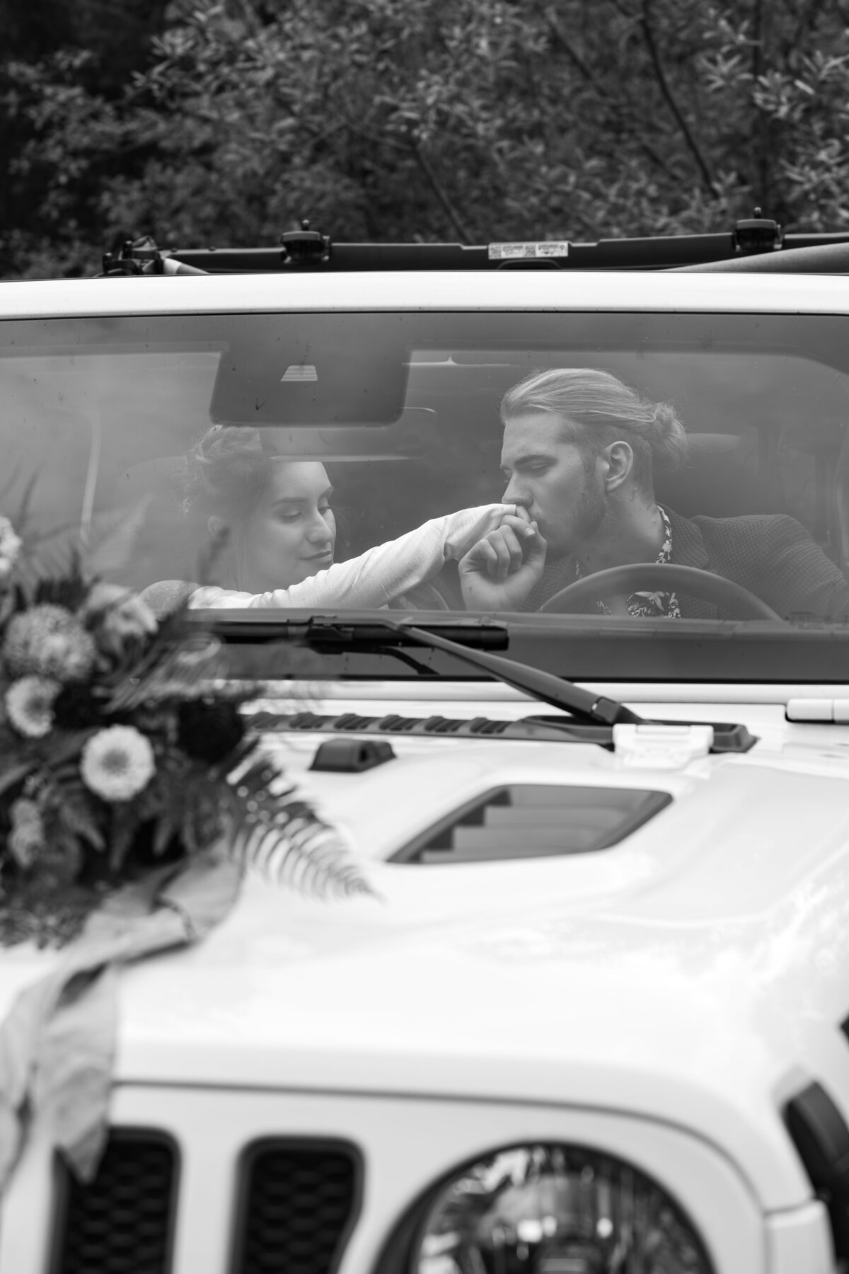 A couple sitting in a jeep as one kisses the other's hand