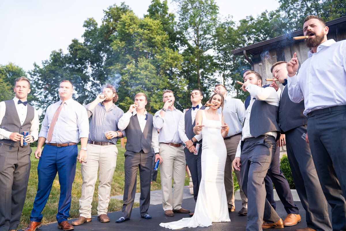 Group of groomsmen and friends smoking cigars with the bride, Mahalie Bee, at a wedding at The Old Blue Rooster Event Center LLC in Lithopolis, Ohio.