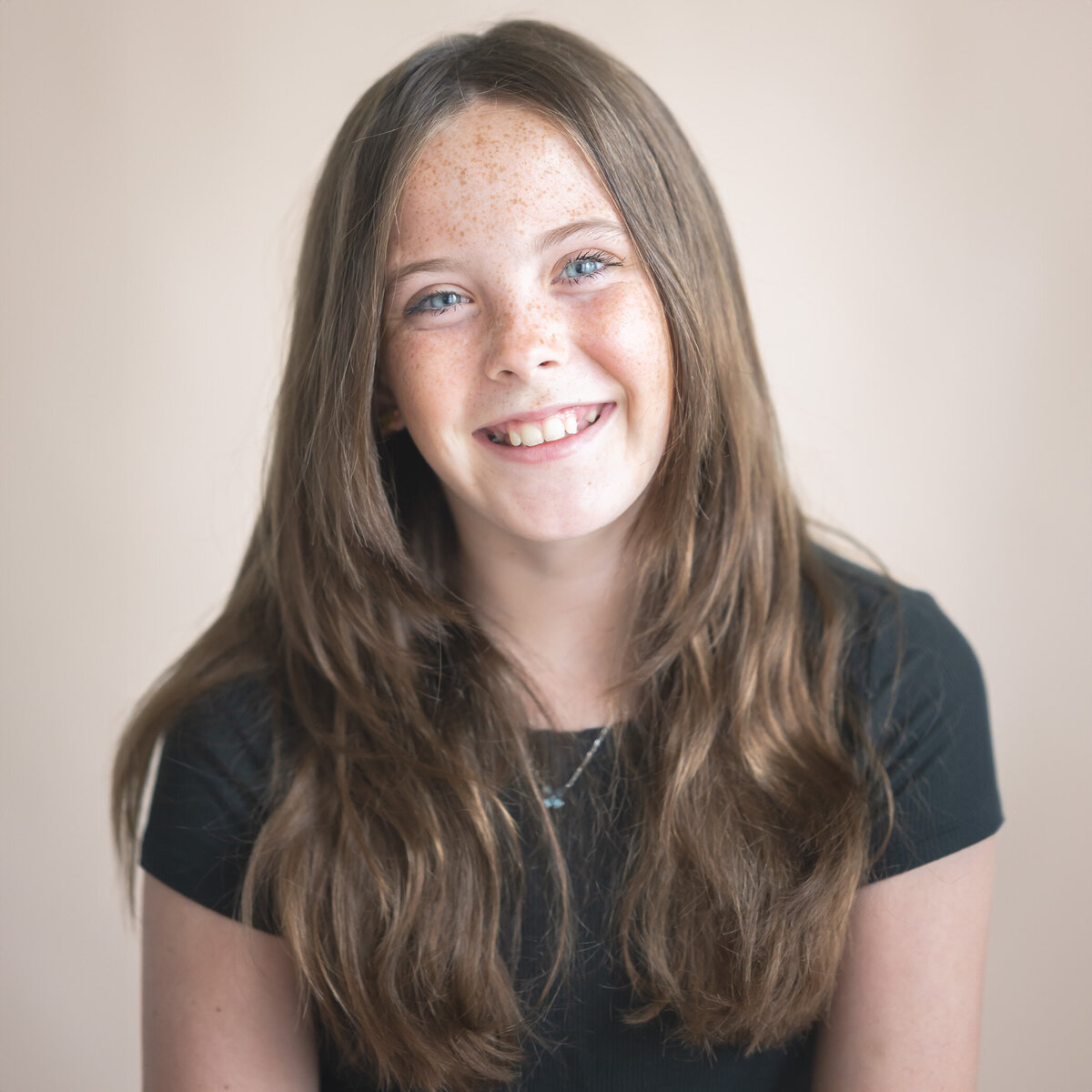 11 year old smiling and tilting head against a light tan backdrop