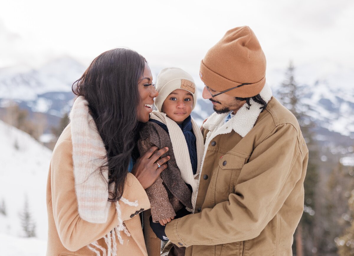 Family of three snuggles close together in jackets and hats on a winter day for a Breckenridge Family Photographer