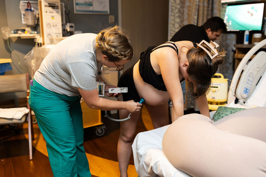 A midwife checks the fetal heartbeat whole a birthing person bends over in a contraction