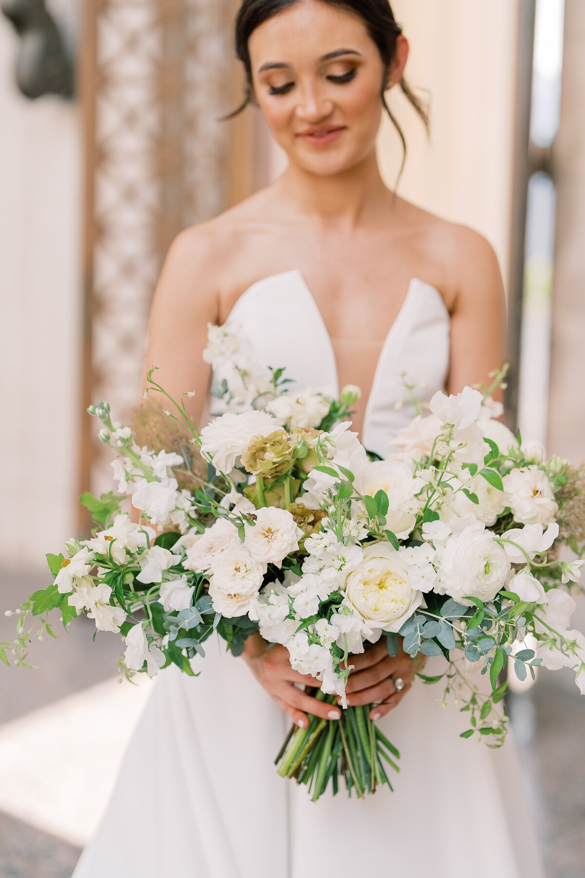 Whimsical bridal bouquet in cream, white, taupe, and champagne colors. This summer wedding bouquet is full of fun texture and represents elegant and timeless floral design. Composed of roses, lisianthus, smoke bush, ranunculus, and natural greenery. White and green floral wedding in downtown Nashville. Design by Rosemary & Finch Floral Design in Nashville, TN.