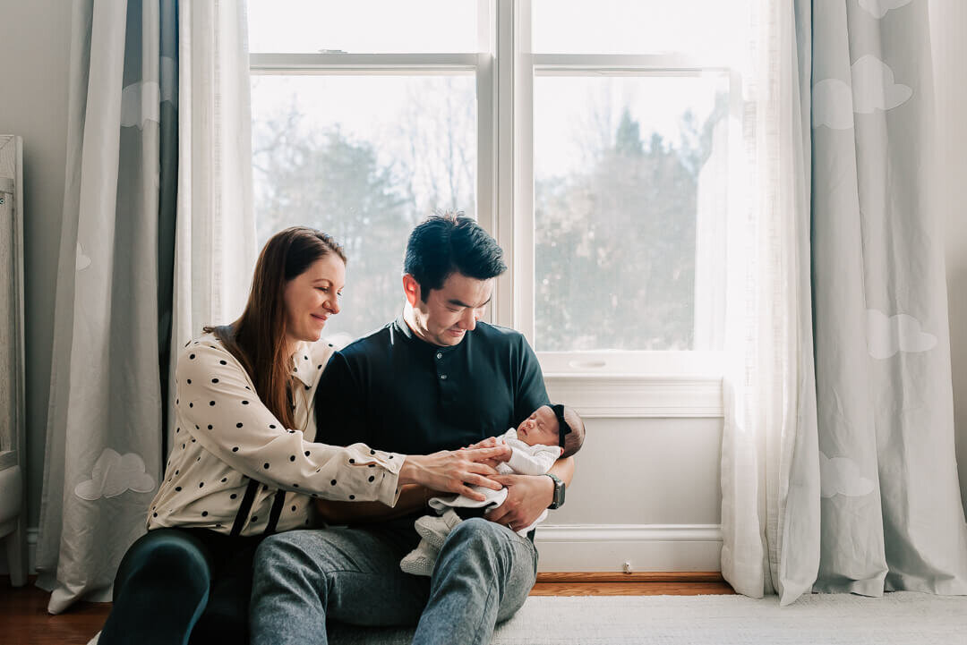 mom and dad sitting under a sunny window holding their baby girl by denise van photography