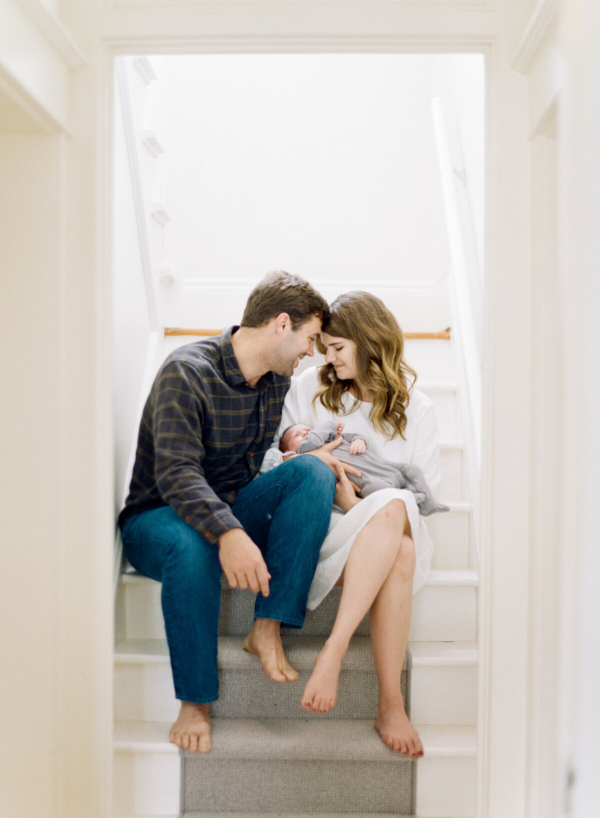 New parents sit on the stairs and snuggle their baby. Image by Raleigh newborn photographer A.J. Dunlap Photography.