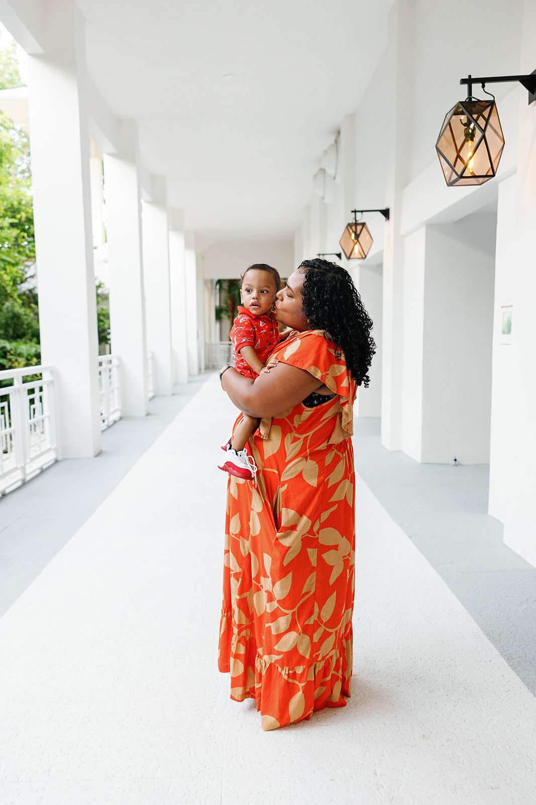 A mother in a flowing orange dress embraces her baby in a softly lit hallway during a Florida Keys family photography session.