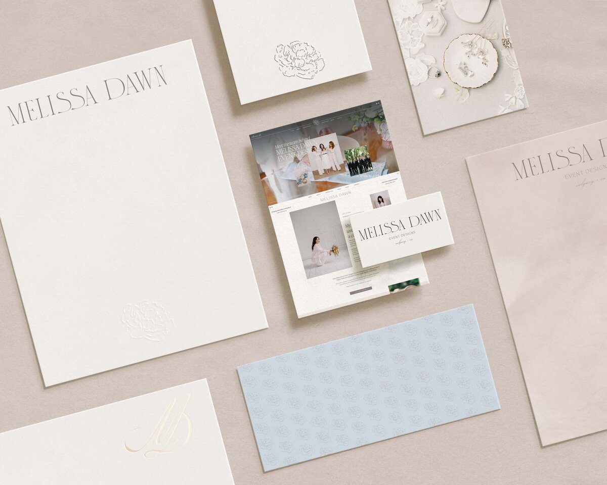 An arrangement of various elegant stationery items, including envelopes, cards, a brochure, and a wedding photo layout—all showcasing the Melissa Dawn brand identity design services.