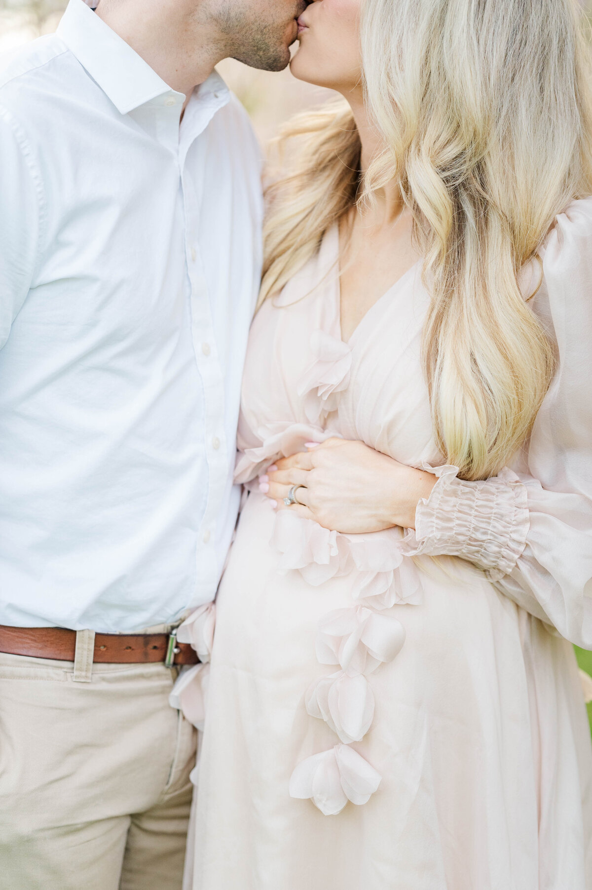 Husband and wife kissing while wife holds pregnant belly in Bristol, RI at Blithewold Mansion taken by best Maternity photographer in Rhode Island