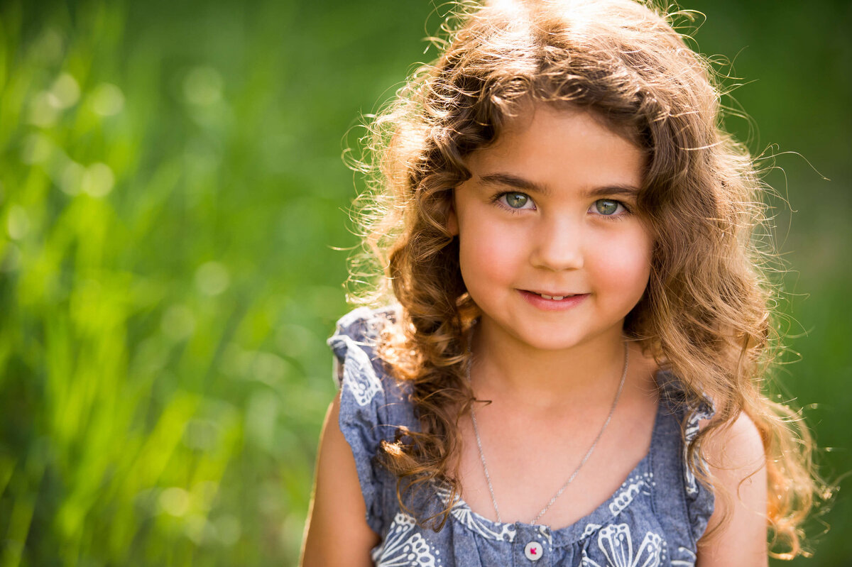 Ottawa Family Photography of a young  girl with curly hair and blue eyes taken outside in a grassy field
