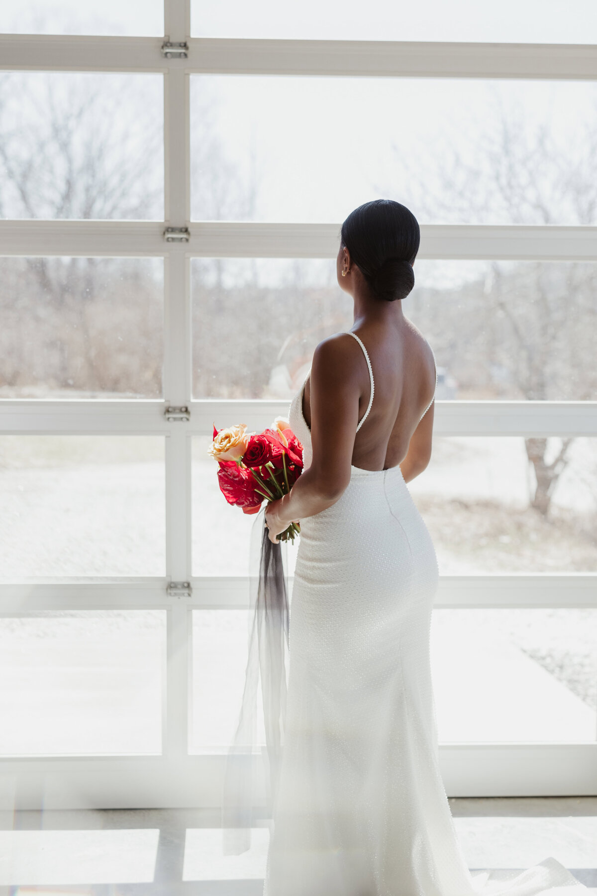 The bride in white, holding her bouquet while she looks outside of the wedding venue