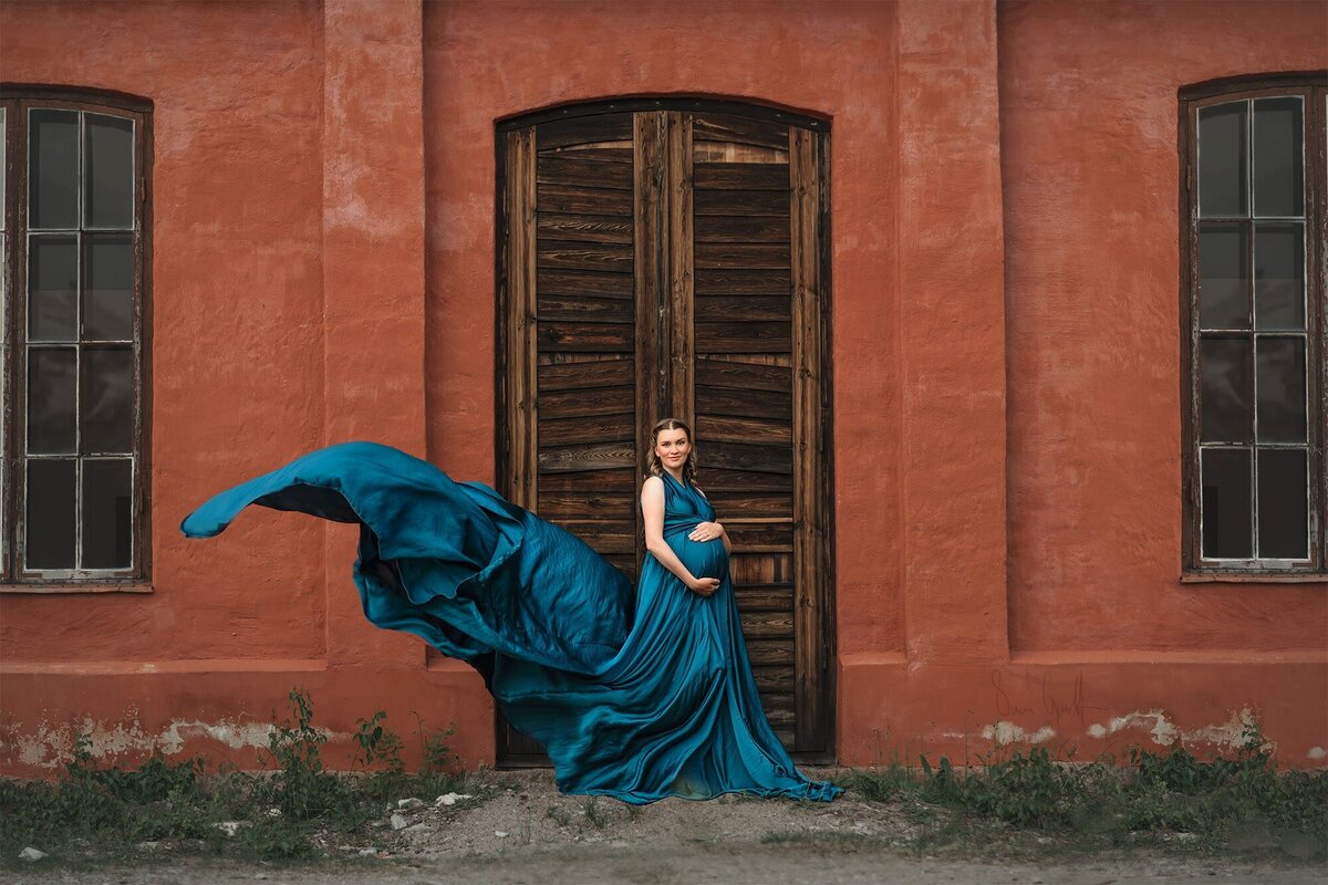 gravidfotografering i en vacker petrolblå böljande klänning framför ett orange gammalt hus.