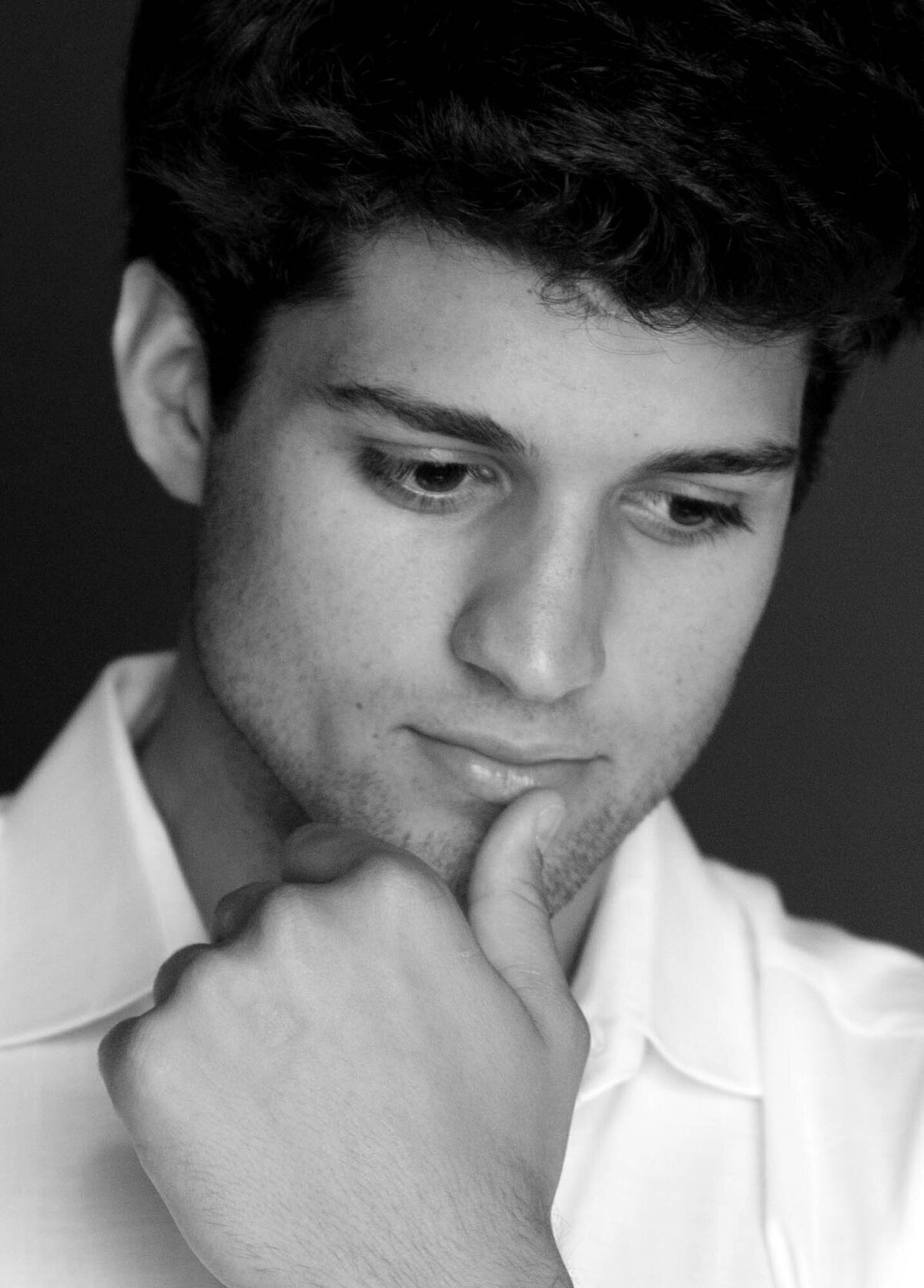 Black and white photo of a man in a white shirt looking down thoughtfully, hand on chin. The tone is contemplative and introspective.