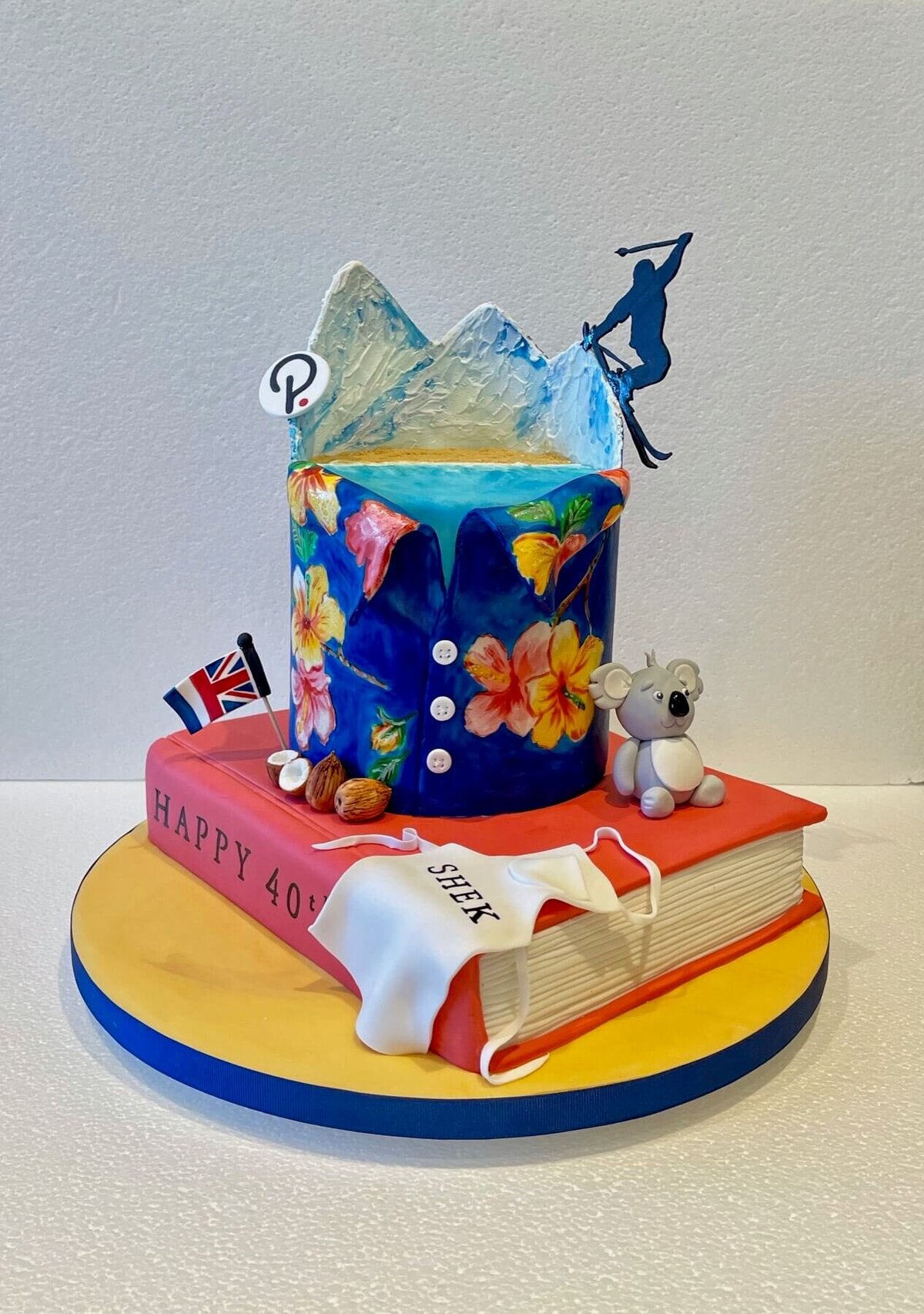 A custom birthday cake with a book, apron, koala, flag and floral shirt