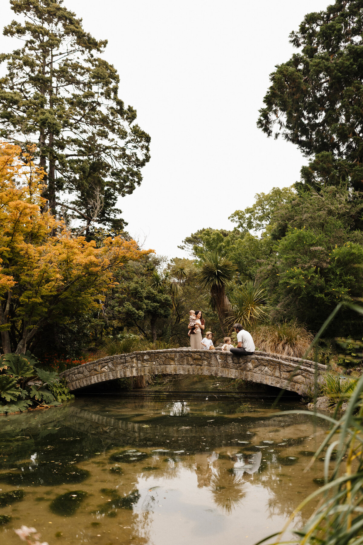 A family sitting on a bridge during a lifestyle family photoshoot at a christchurch park