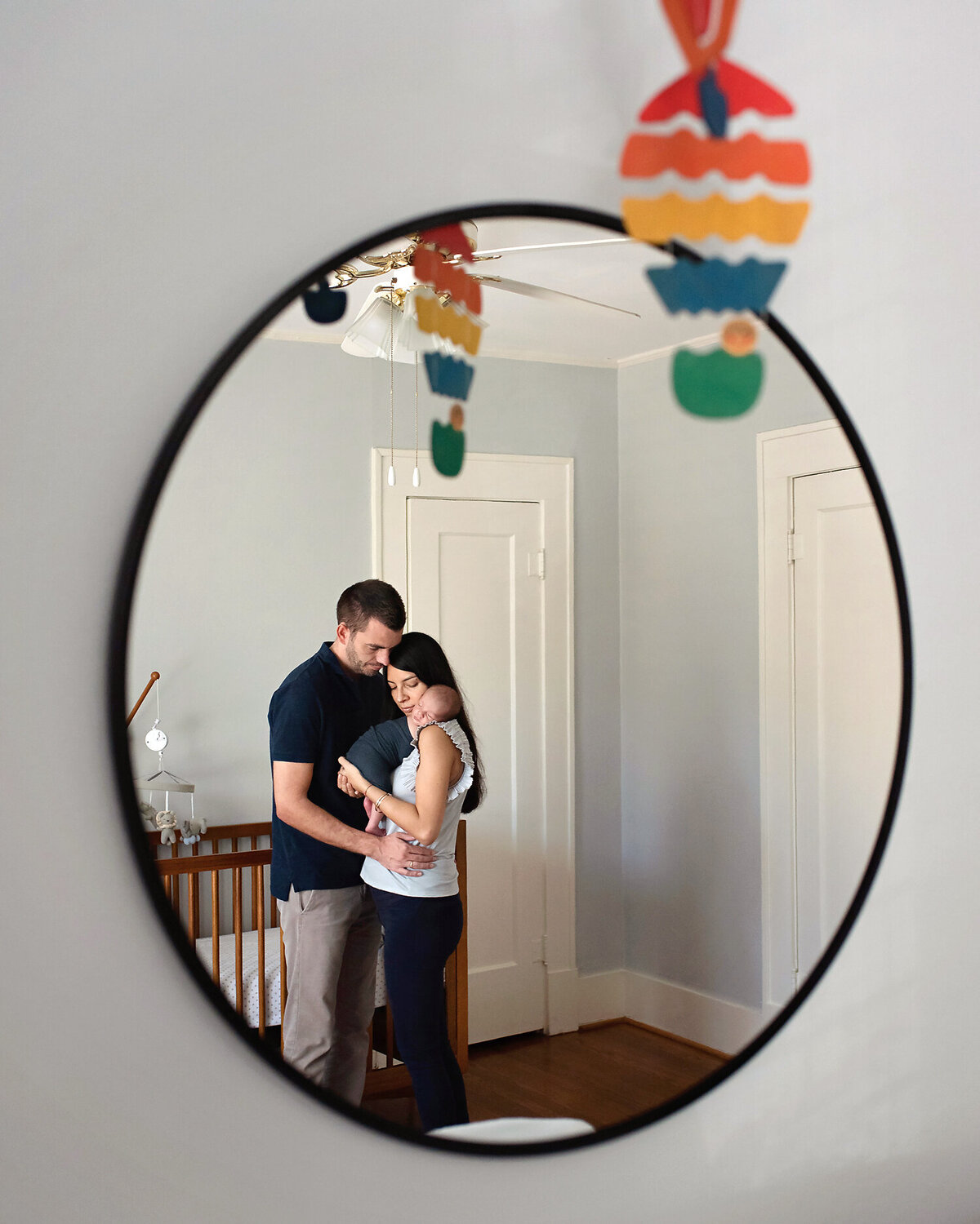 A reflection in the mirror of new parents holding their baby boy in his nursery in Lakewood Heights, Dallas.