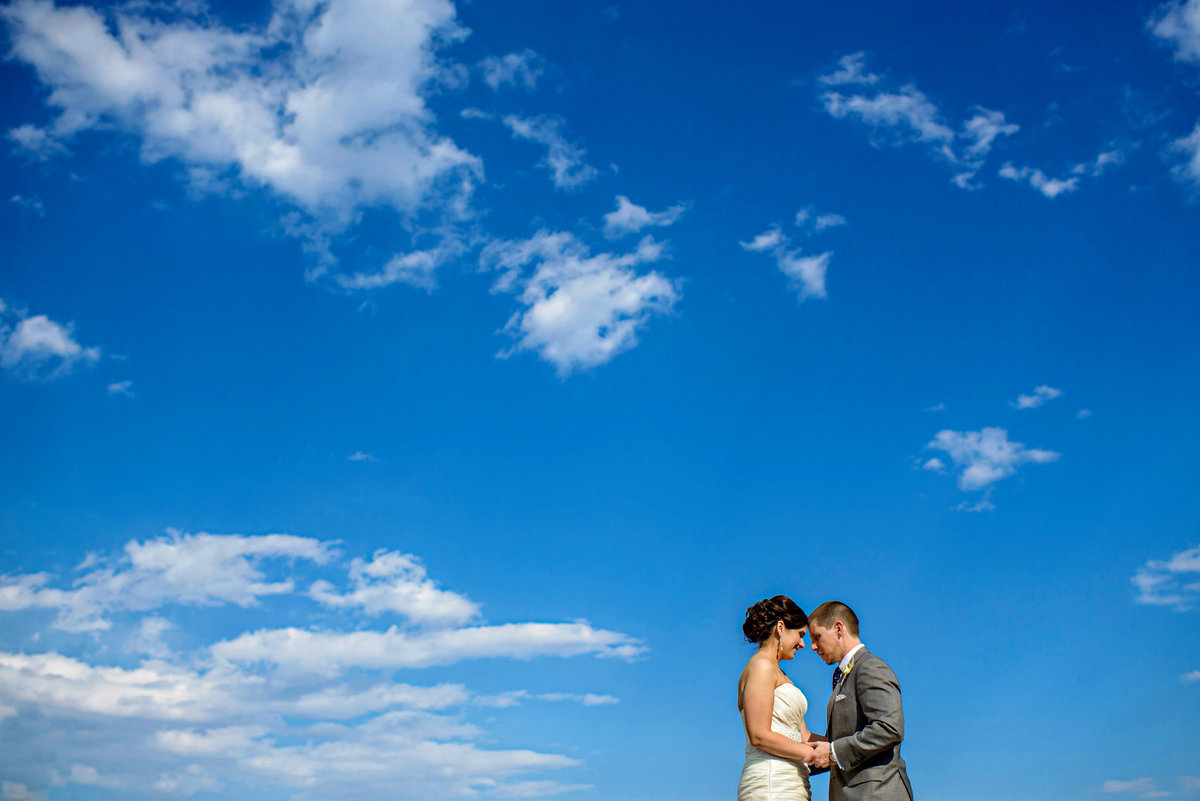 A bride and groom soak in the sun and a blue sky full out fluffy clouds.