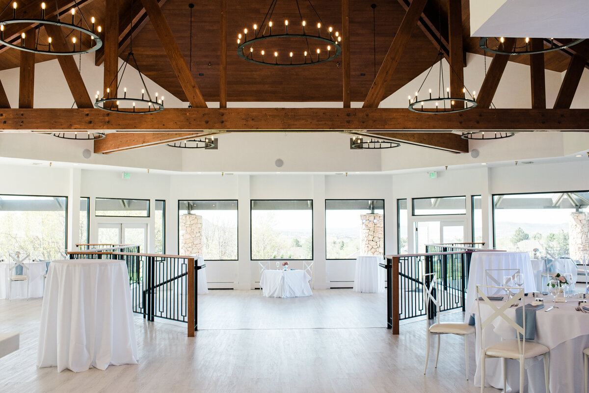 denver wedding venue reception space with dark wooden beams and large hanging chandeliers in addition to a large wall of windows photographed by denver wedding photographer