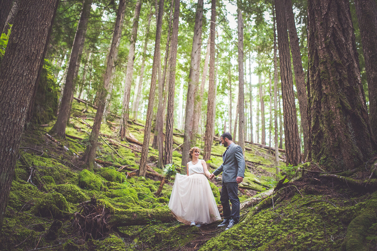 Bride and groom walk through the tall forest trees on their elopement day.