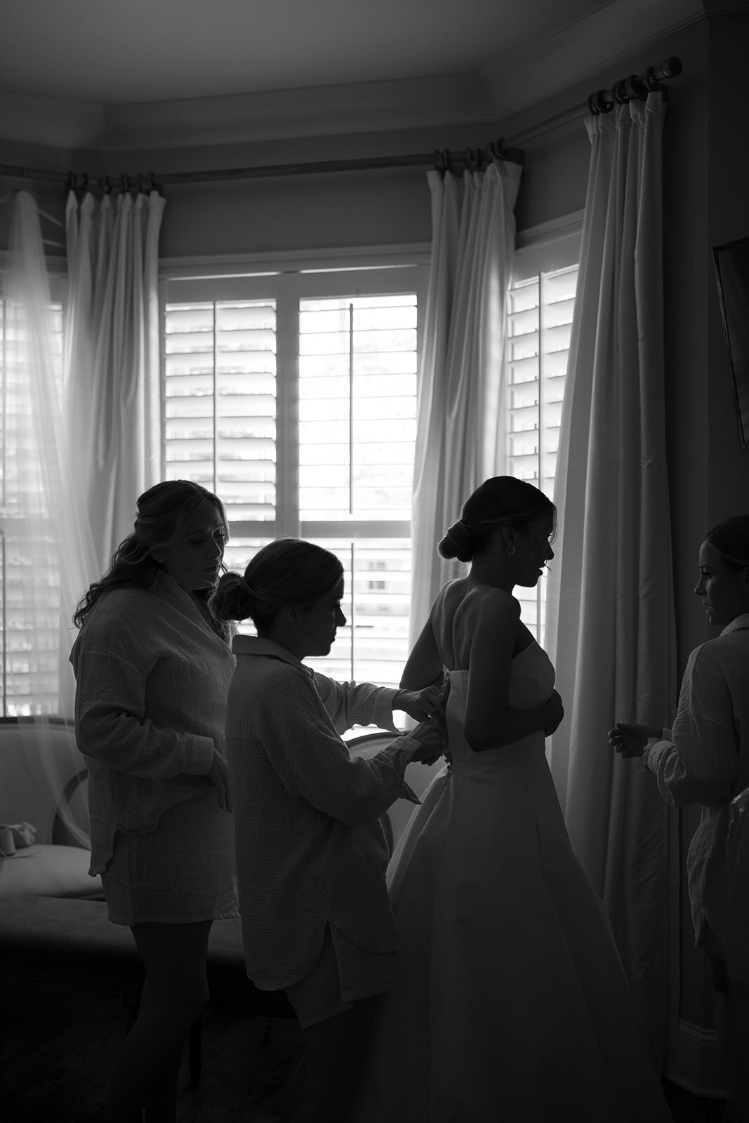 Black and white photo of the bride surrounded by bridesmaids as they help her into her wedding gown before the ceremony at Burritt on the Mountain in Huntsville, Alabama, photographed by Perry Hancock.