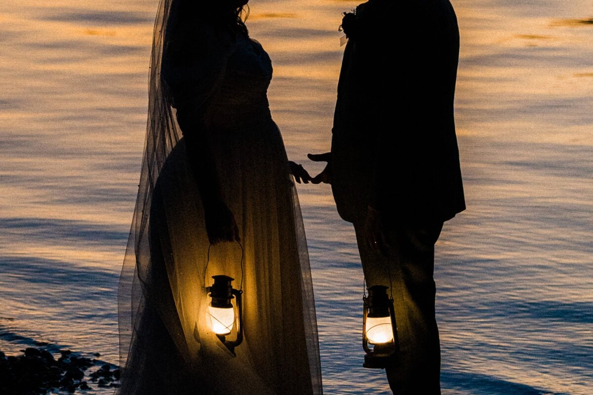 2 hands lightly touch with golden lanterns and sunset kissed water at an Olympic National Park Elopement.