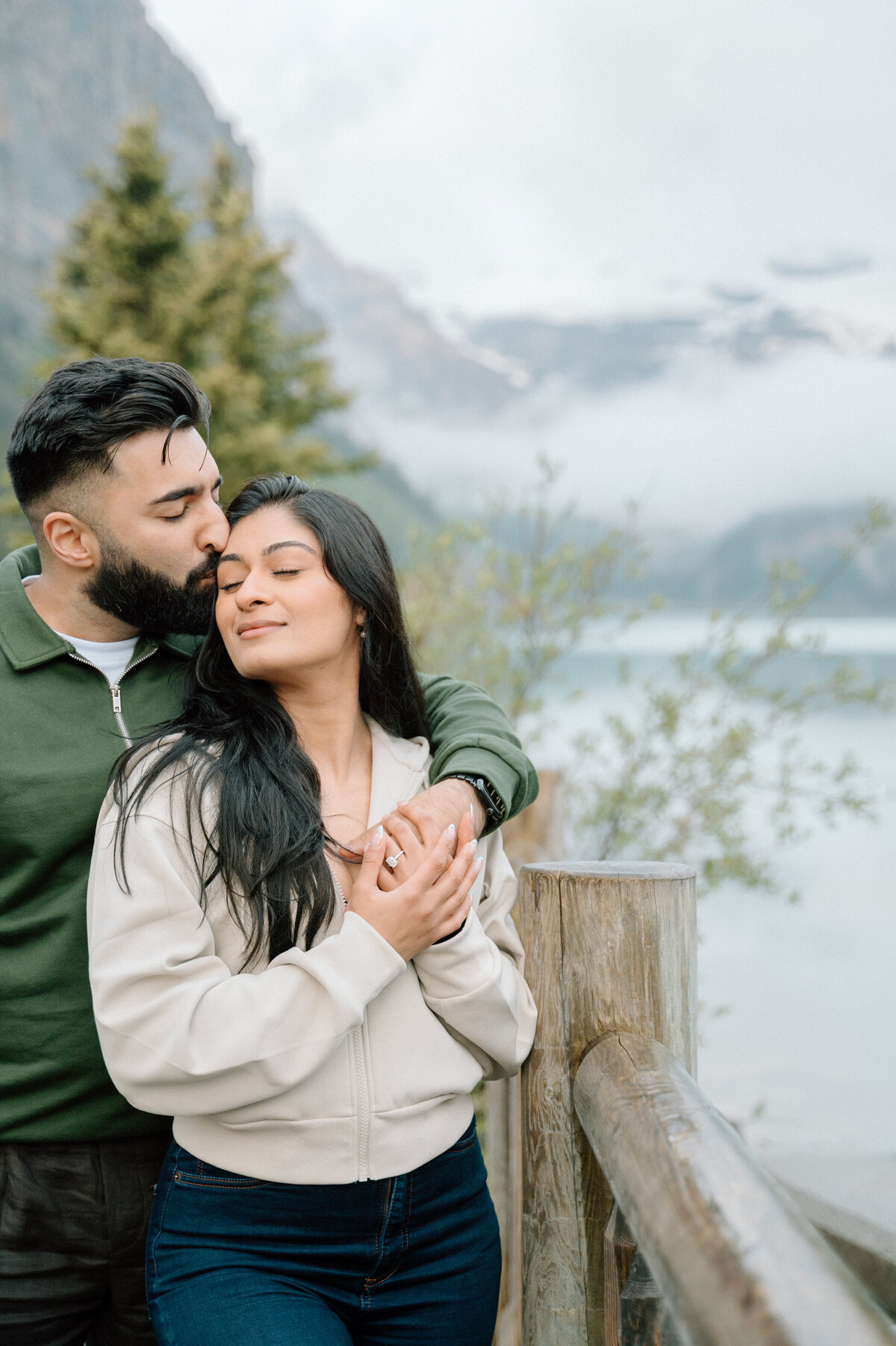 Candid engagement moment with couple embracing at Lake Louise with mountain backdrop.