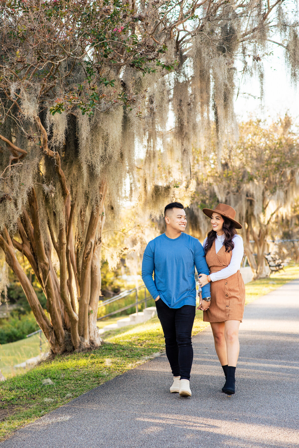 Mixed-race-couple-walking-and-smiling-at-each-other-on-the-sidewalk-under-mossy-trees-of-Riverfront-Park-in-Columbia-SC