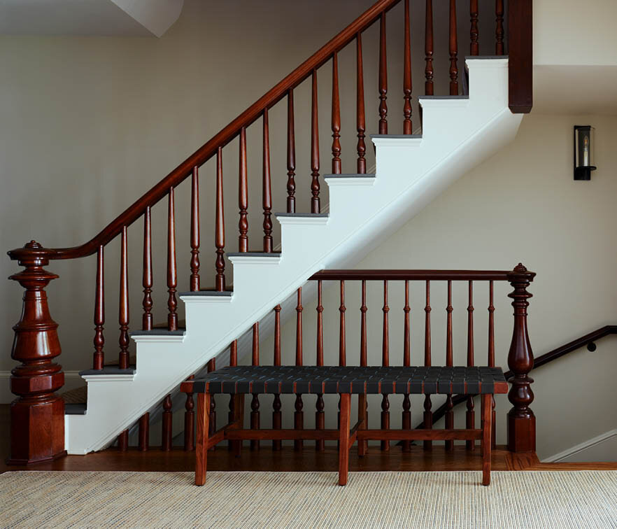 Preserved historic staircase with natural wood railings, white stringers, and stained treads. Simple lighting enhances the original architecture. By Sarah Scales.