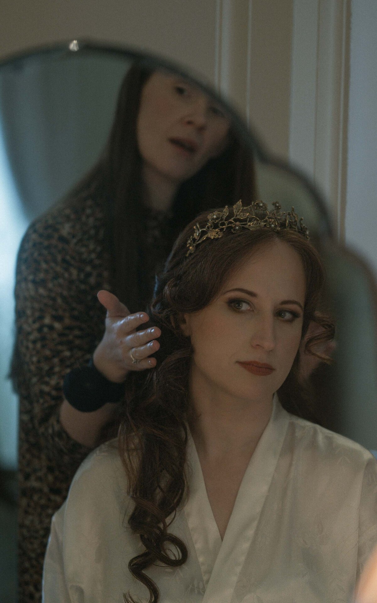 Captured in a serene moment, the bride sits by the mirror, reflecting on her special day while preparing for the wedding ahead