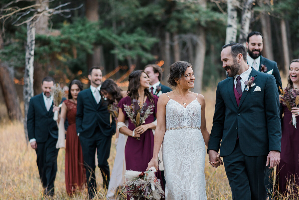 denver wedding photographer captures outdoor wedding with bride and groom walking through the woods with their bridal party for their rocky mountain national park wedding