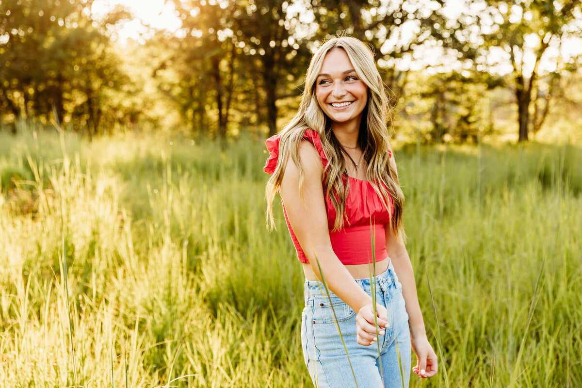 gorgeous brown haired high school teen playing with tall grass as she looks over her shoulder in a field near Oshkosh