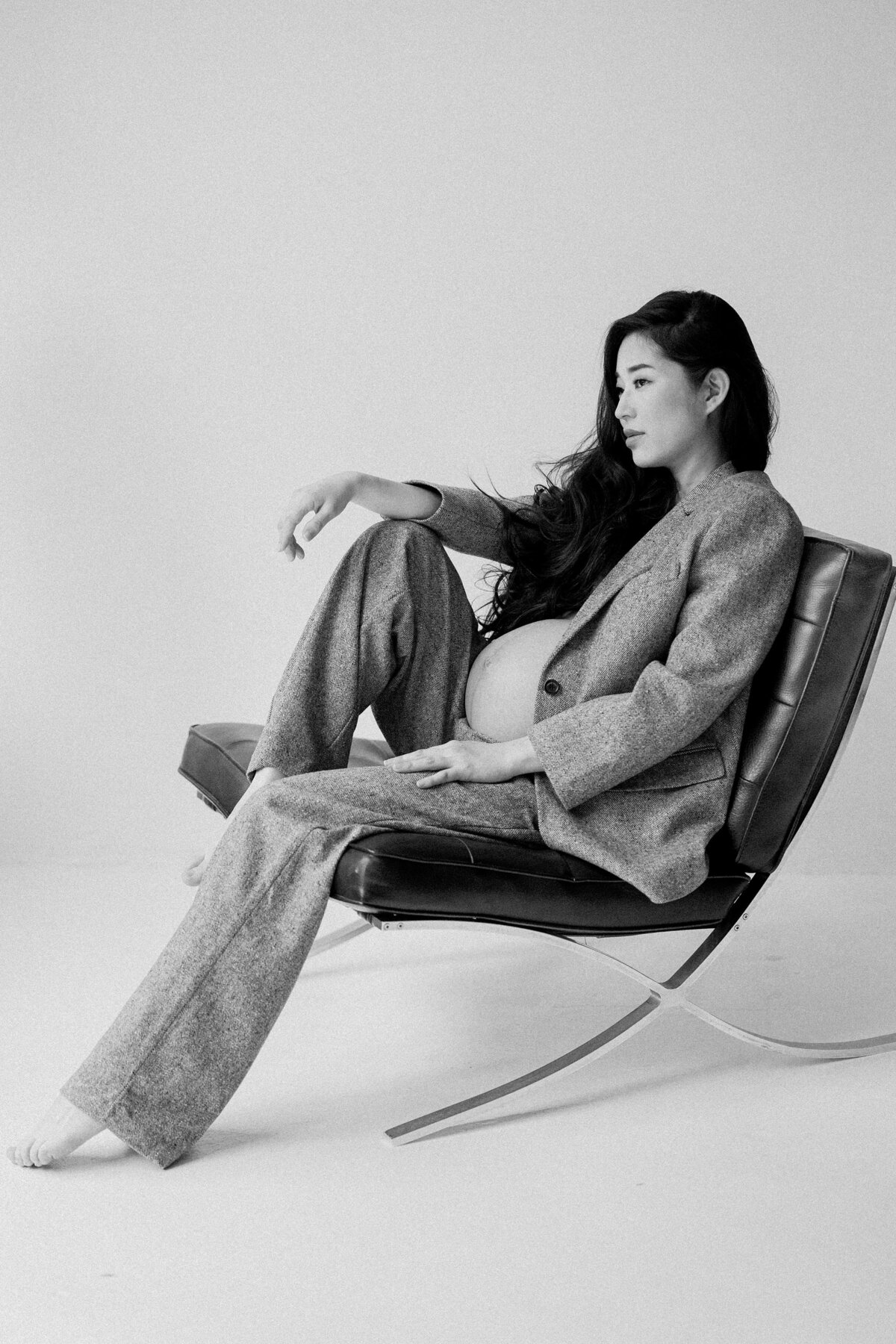 Pregnant woman poses in chair wearing a tweed paint suit during Brooklyn studio session.