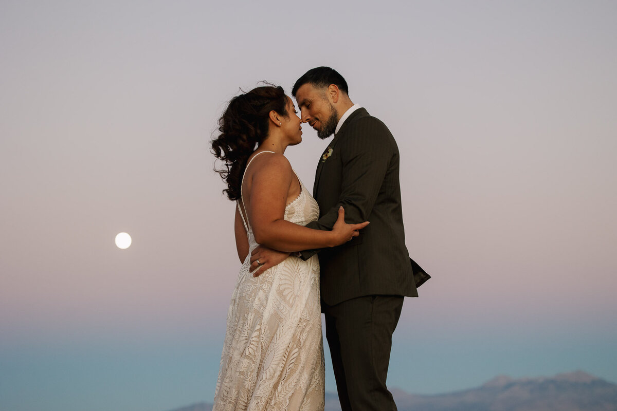 A bride and groom stand nose to nose in an emotional pose as a super moon rises during their Moab elopement