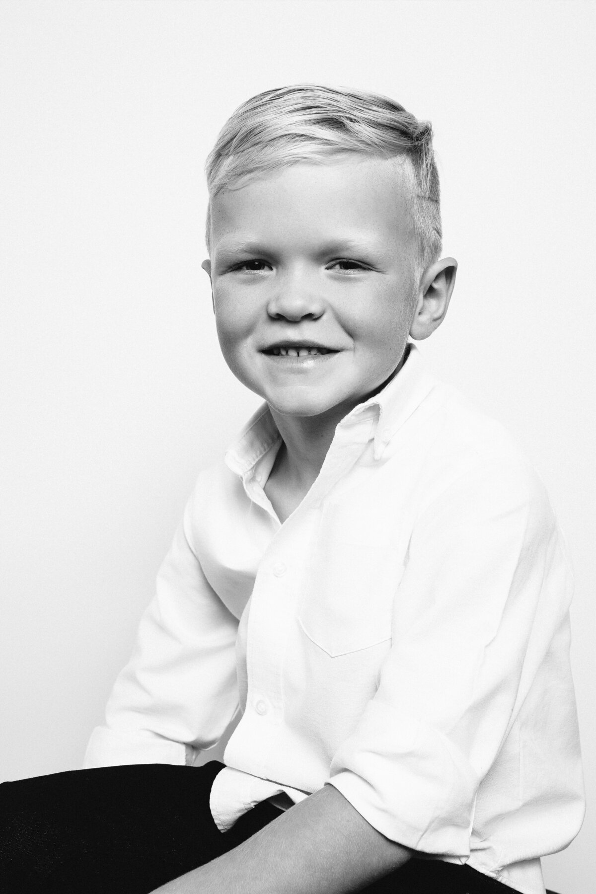 Closeup Black and White photo of young boy wearing white button-down shirt. Sitting down and smiling.