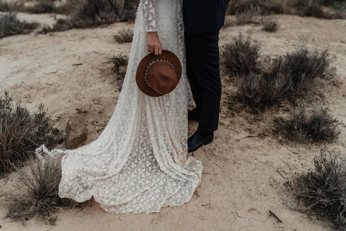 bride-holding-hat-groom-standing-near-bushes