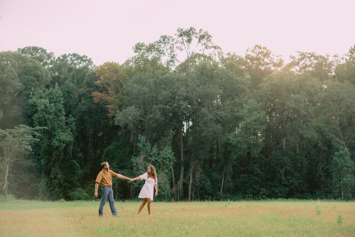 woman guides her fiance by the hand through a field