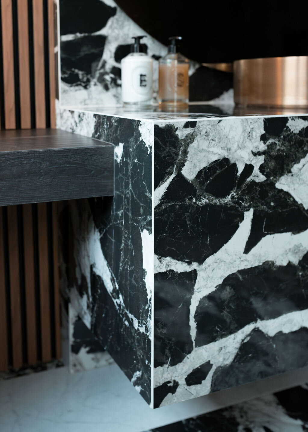 A close-up view of the marble countertop in a dark, modern bathroom. The marble extends to the flooring. To the left, there is a wooden slatted wall.