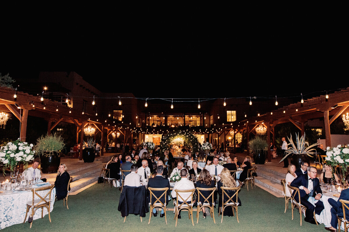 An elegant outdoor wedding reception under the stars, featuring beautifully decorated tables, ambient lighting, and a stunning floral arch.