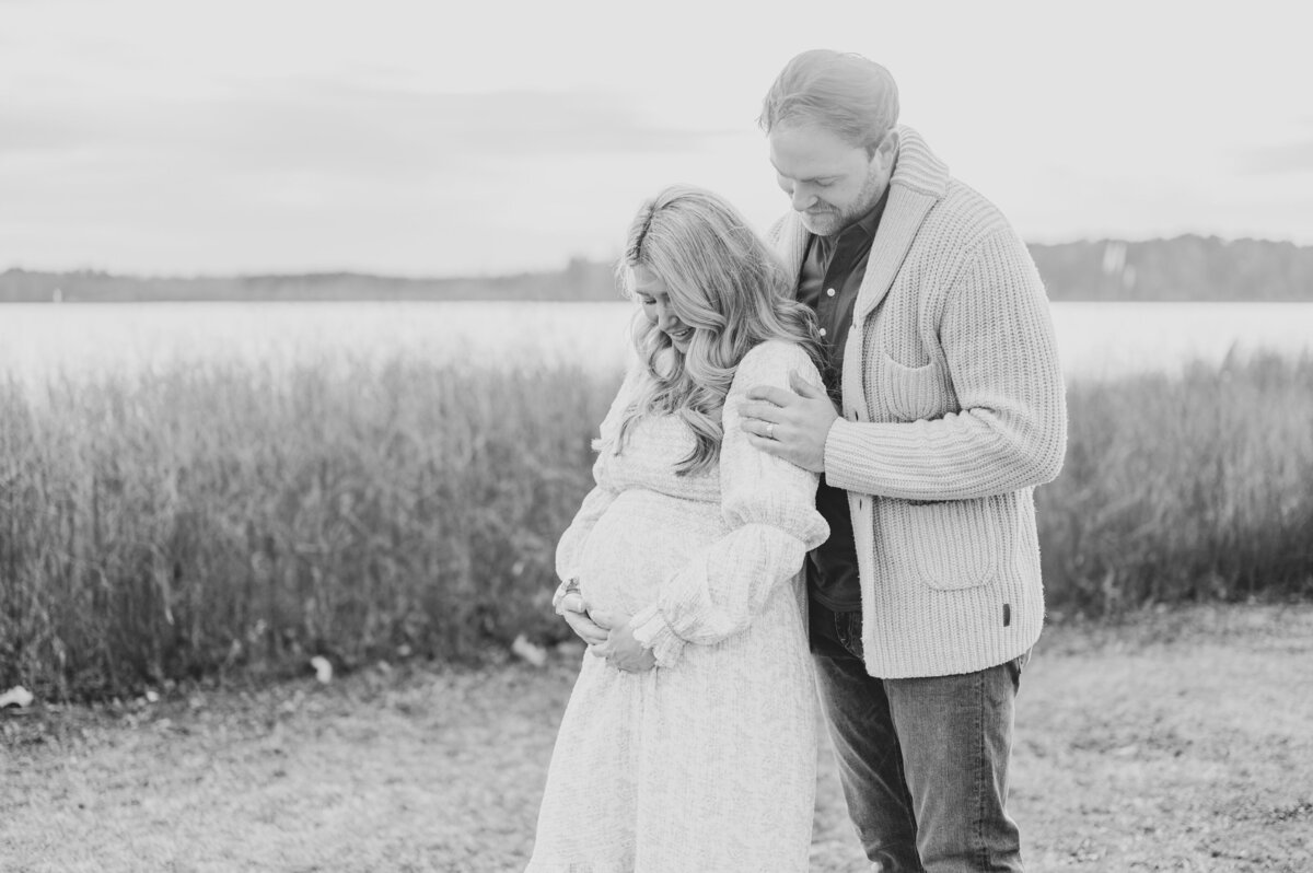 Expecting couple stands in front of lake in black and white maternity photos