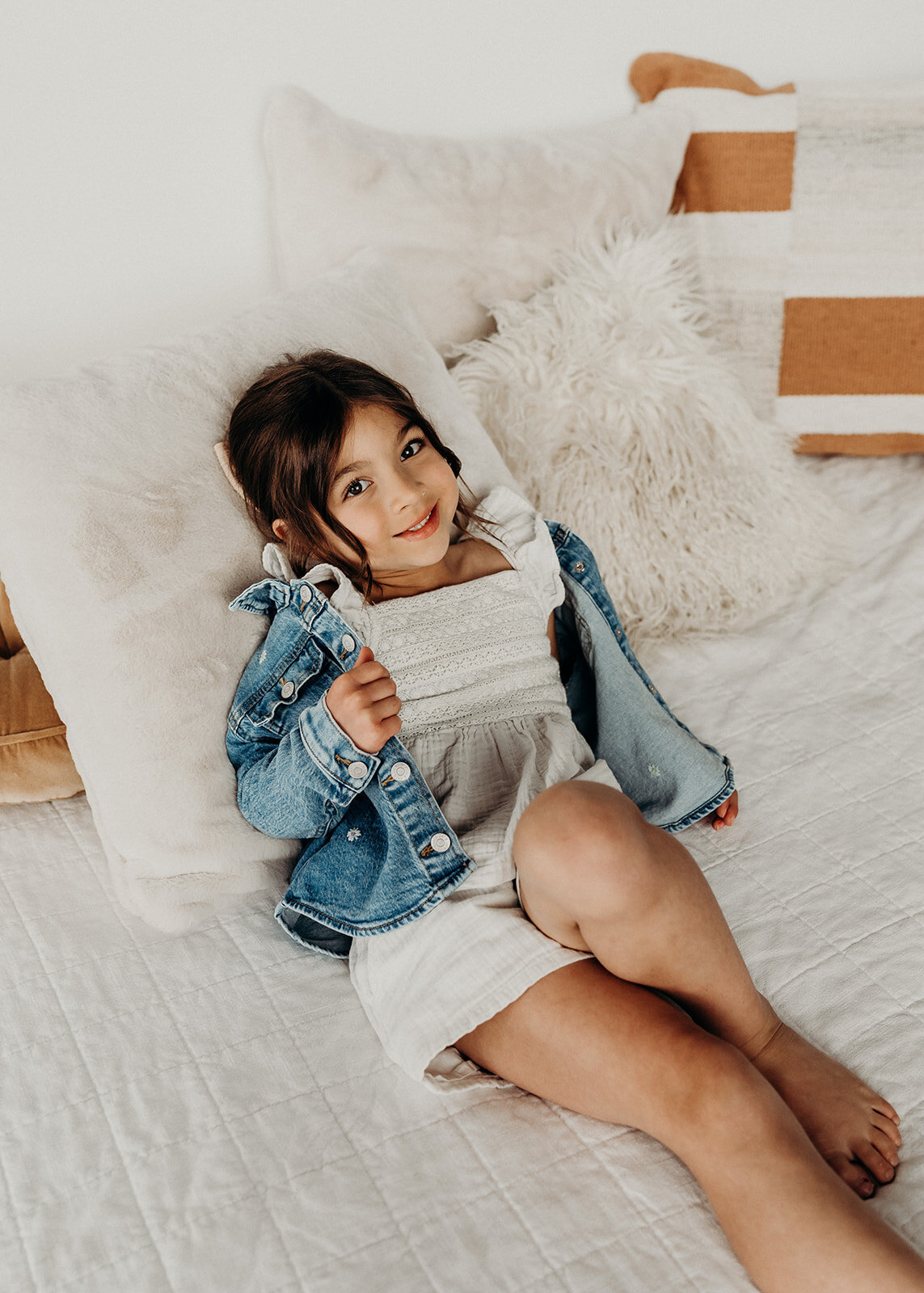 little girl in white and denim  smiles on bed