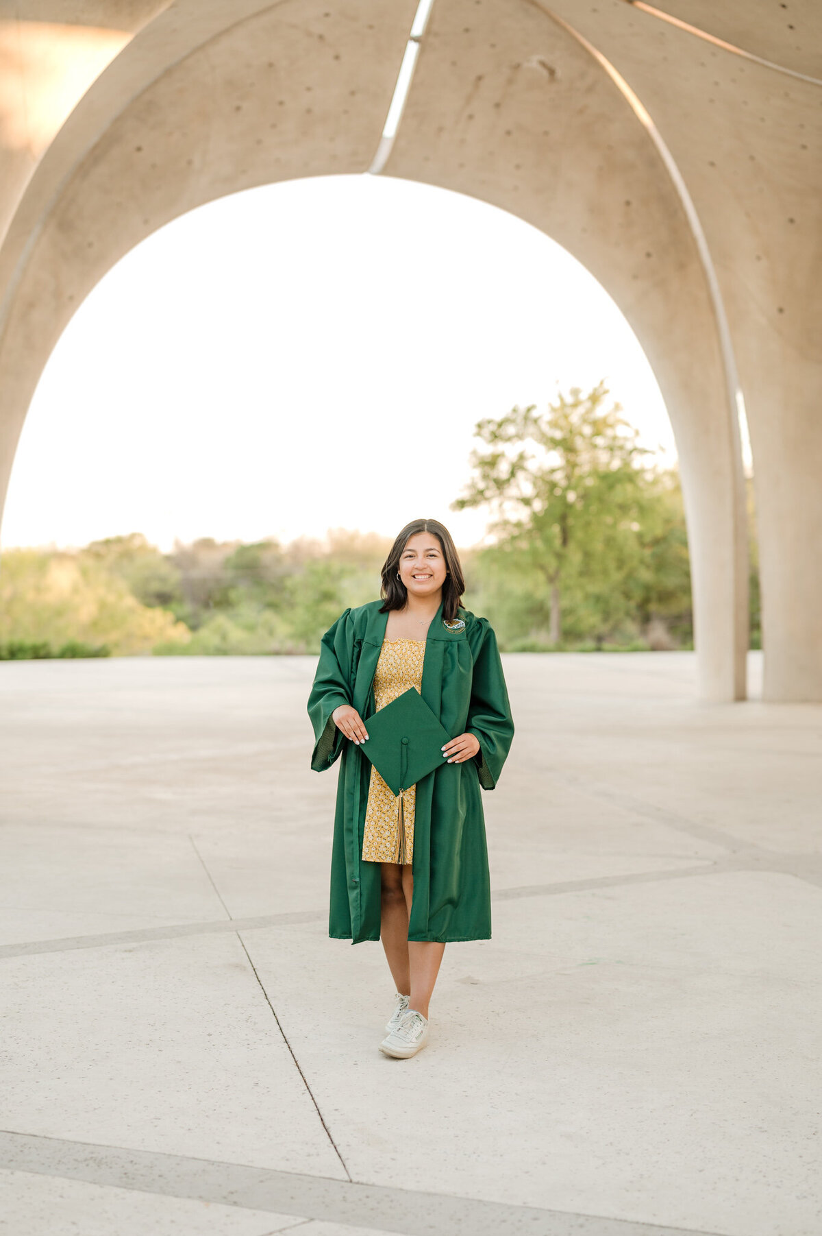 Senior holds her graduation cap and wears her gown at Confluence Park in San Antonio.