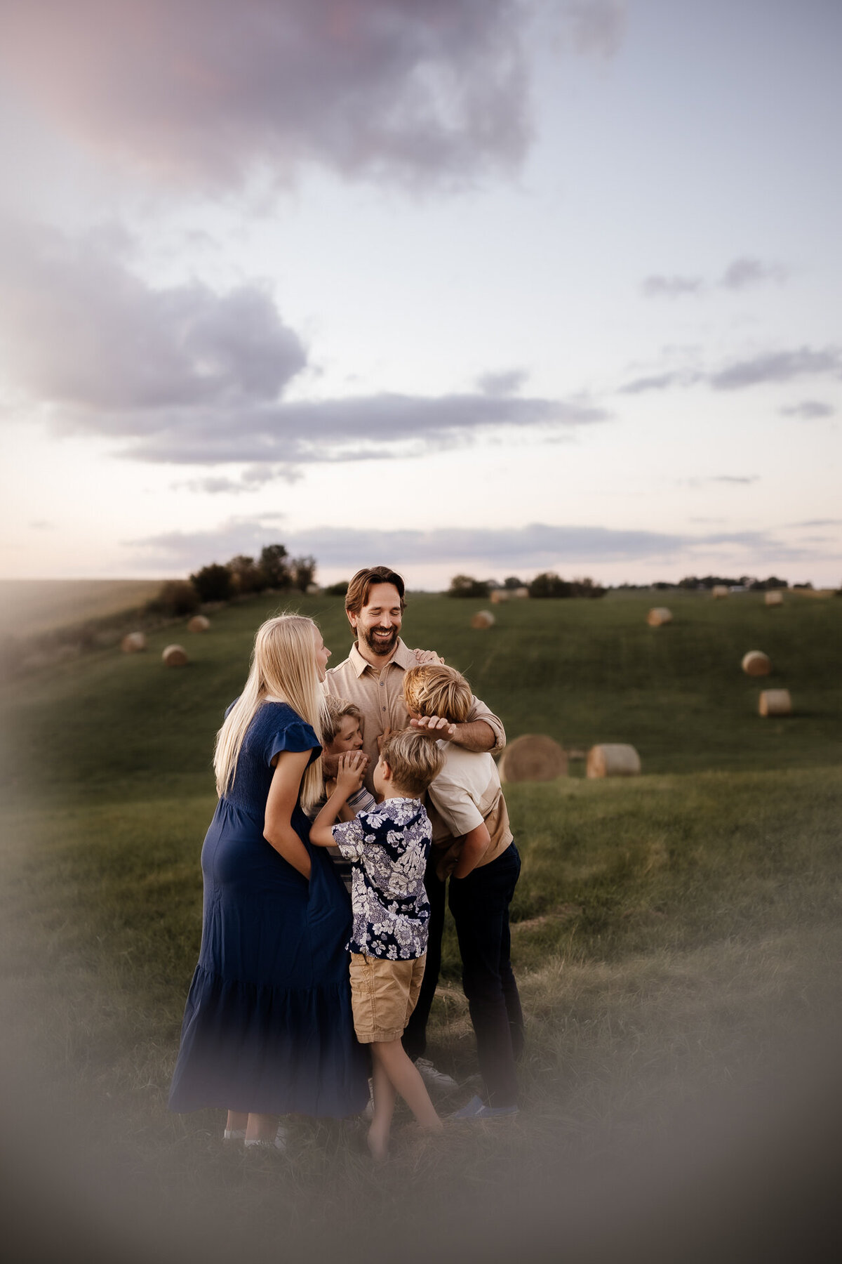 dad and children hugging in hay bale field