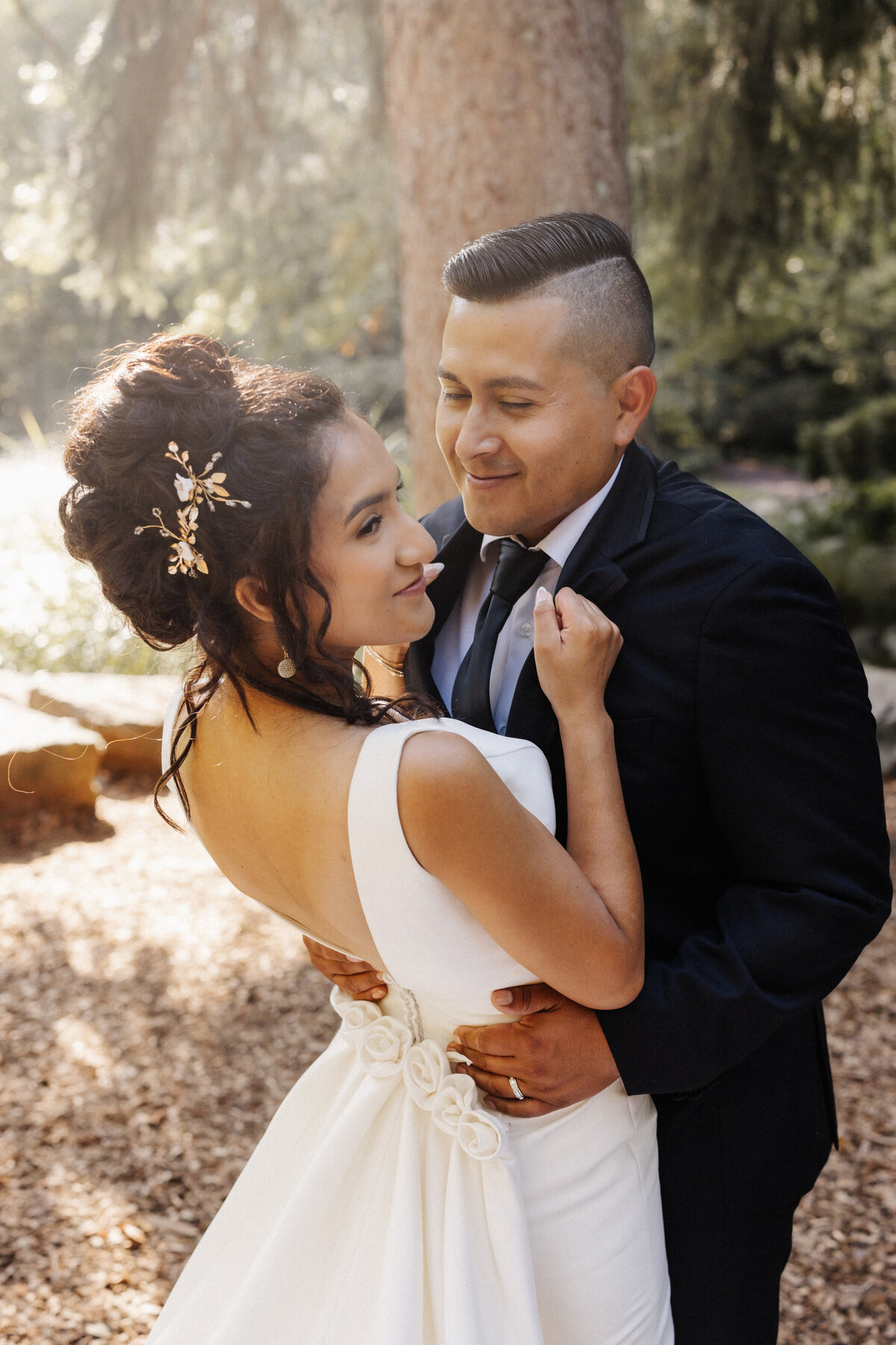 Bride and groom embracing in soft sunlight during an outdoor forest wedding portrait.