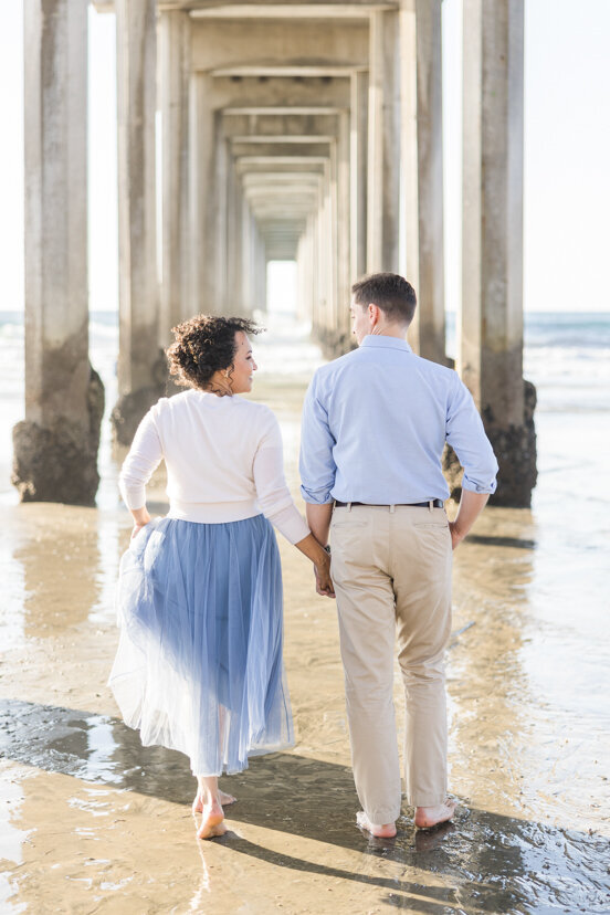 engaged-couple-running-under-Scripps-Pier-San-Diego