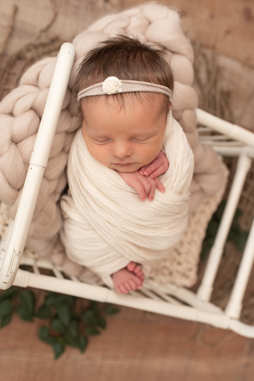 Picture of newborn baby girl wrapped in neutral with white headband in white crib | Sharon Leger Photography