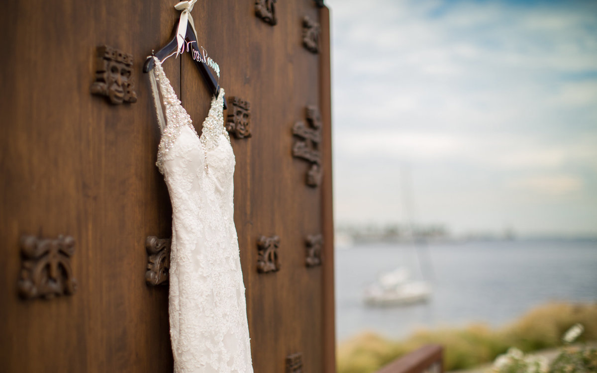 A Bride's dress hangs on display with a boat in the ocean in the background