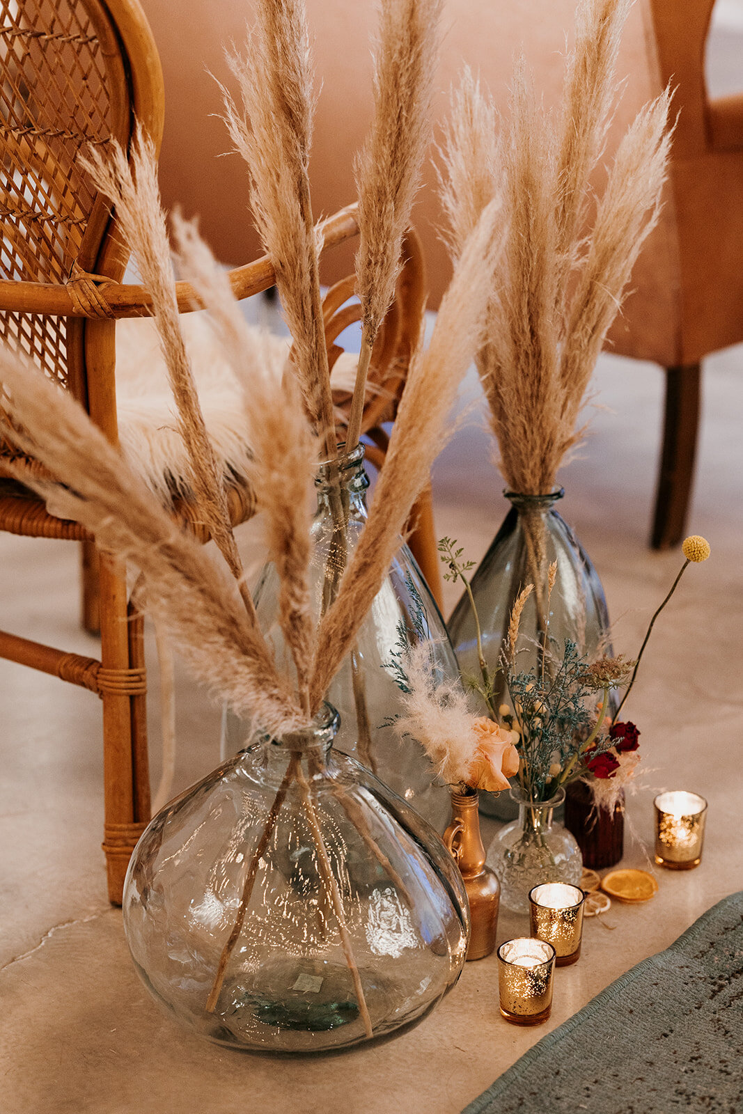 Decorative arrangement of pampas grass in large glass vases, surrounded by small candles and rustic florals, creating a boho-inspired setting.