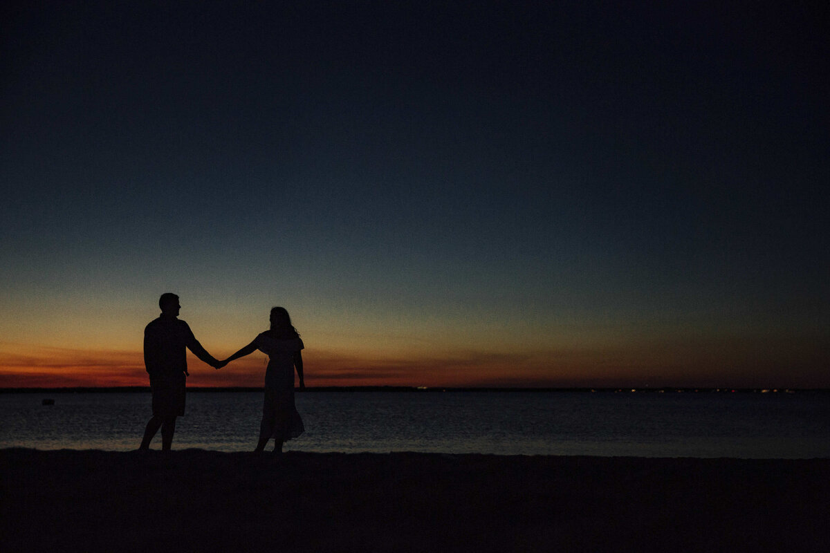 Couple holding hands in beach silhouette at sunset during engagement photo in Point Pleasant New Jersey