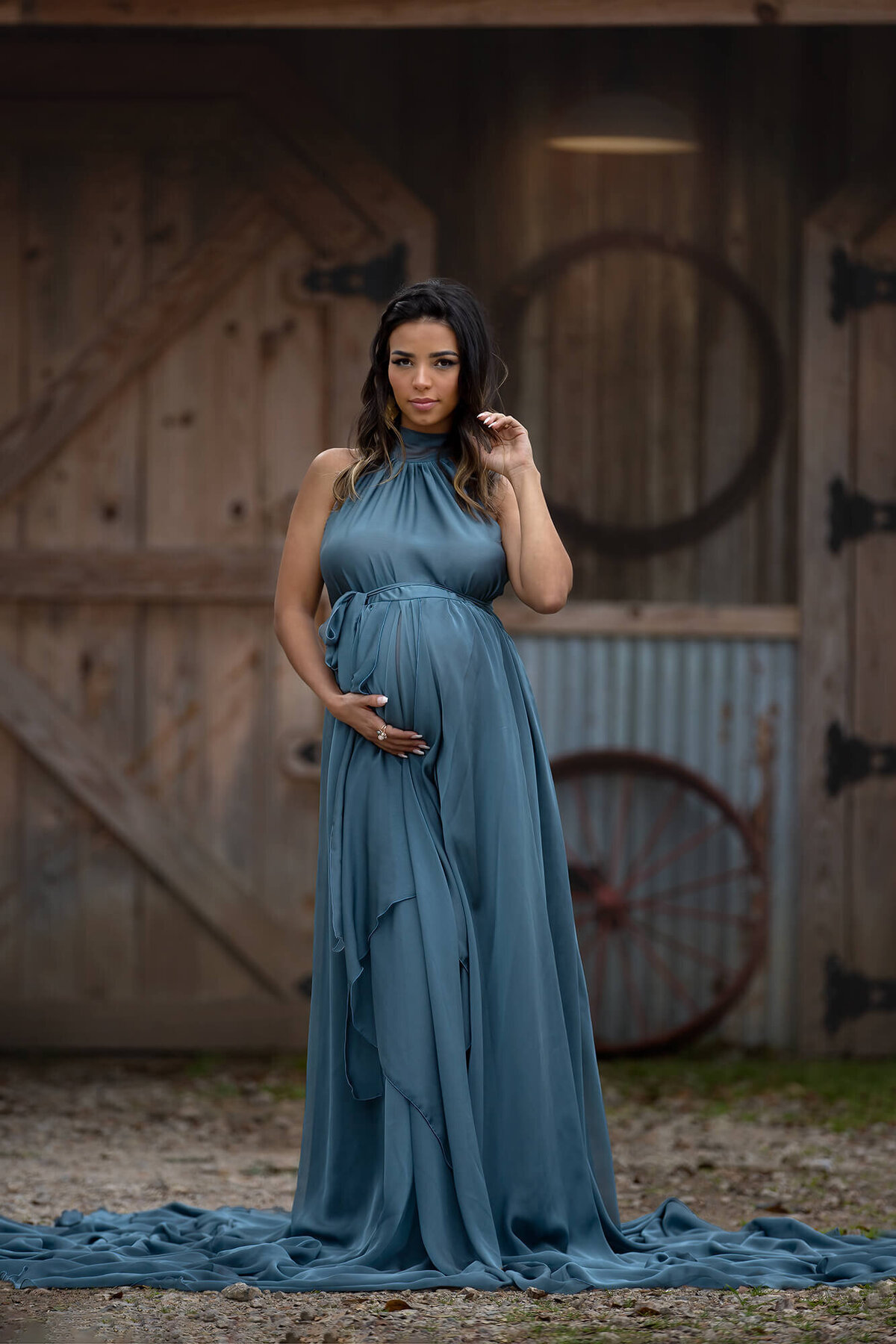 Stunning mom to be wearing a blue dress in front of a barn